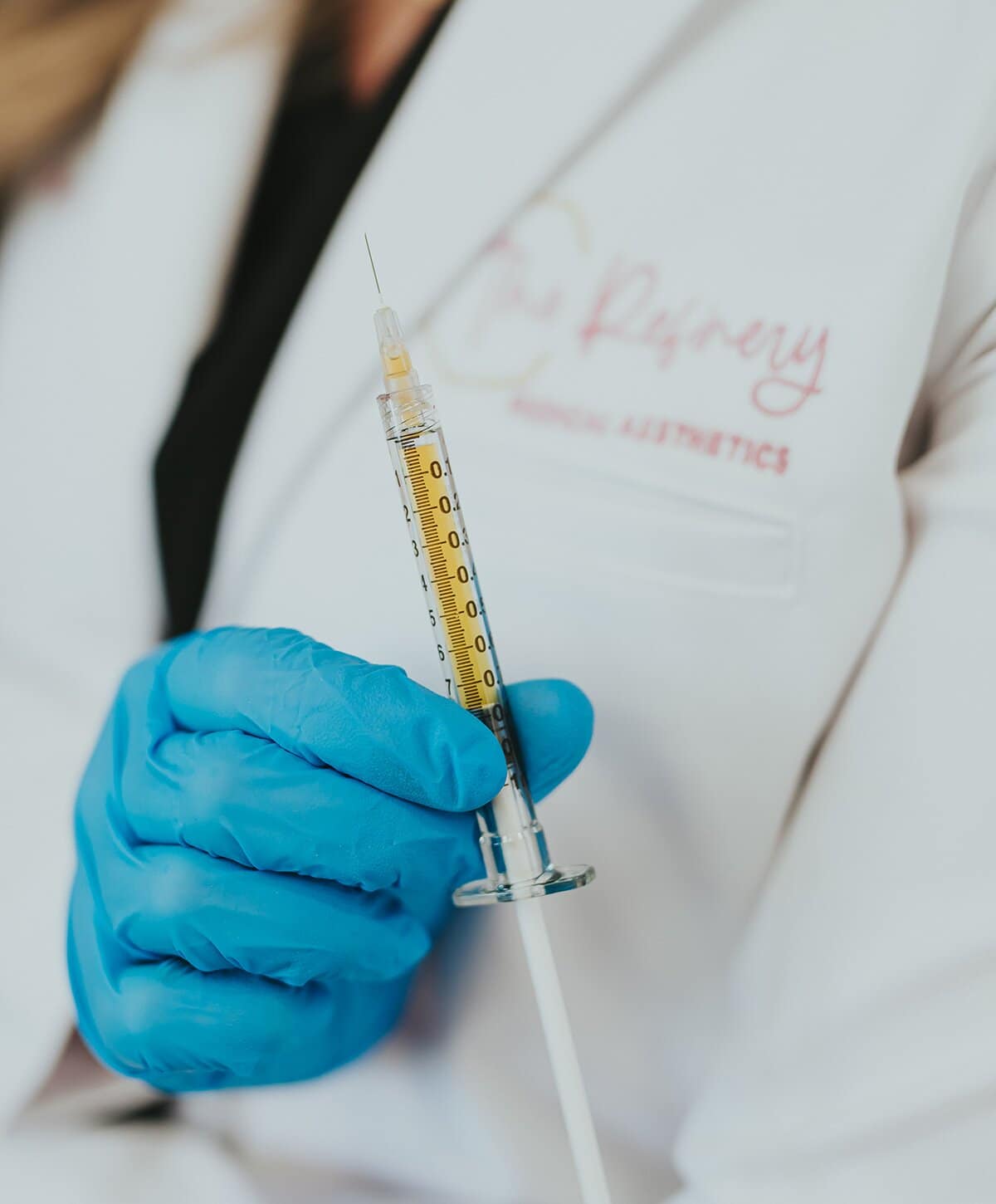 Hand in blue glove holding full syringe